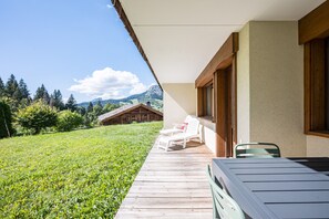 Eine Holzterrasse mit Gartenmöbeln, mit Blick auf eine Wiese und einen Berg im Hintergrund.