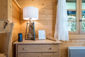 Ein Interieur einer Holzhütte mit Schreibtisch, Lampe, einem begrüßenden Schild im Bilderrahmen und einem Fenster mit Blick auf Grünflächen.