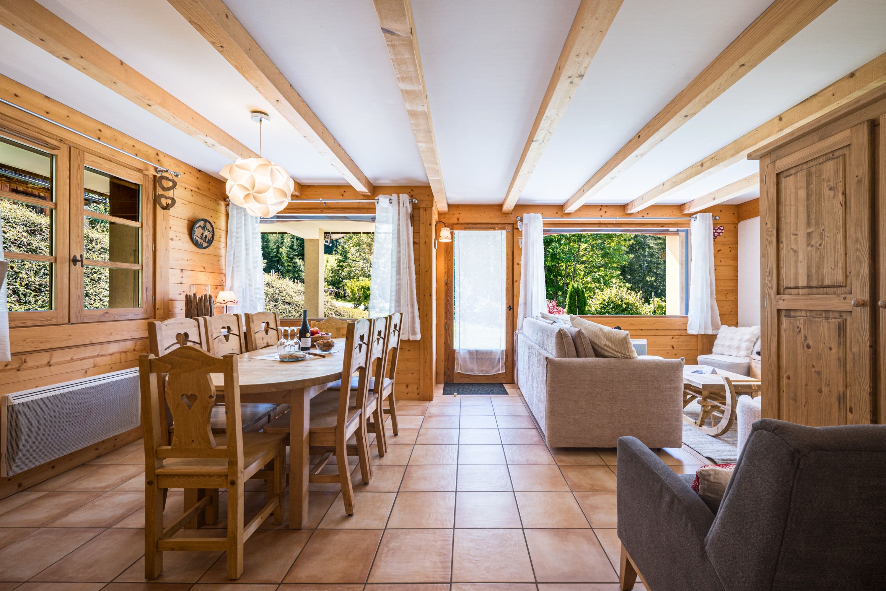 Un intérieur en bois comprenant un coin repas, un canapé et une vue sur la verdure environnante.