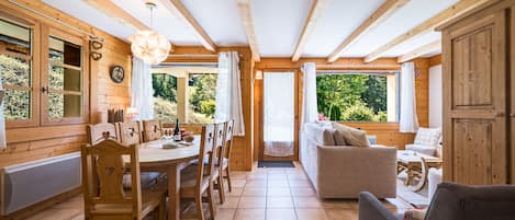 Een houten interieur met een eethoek, een bank en uitzicht op groen.