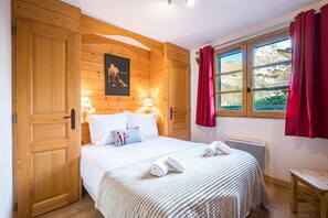 Ein Zimmer aus Holz mit einem Bett, einem Fenster mit Vorhängen und einem Wandbild.