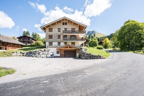 Un edificio de madera de dos pisos con un balcón, un garaje y un muro de piedra en la fachada.