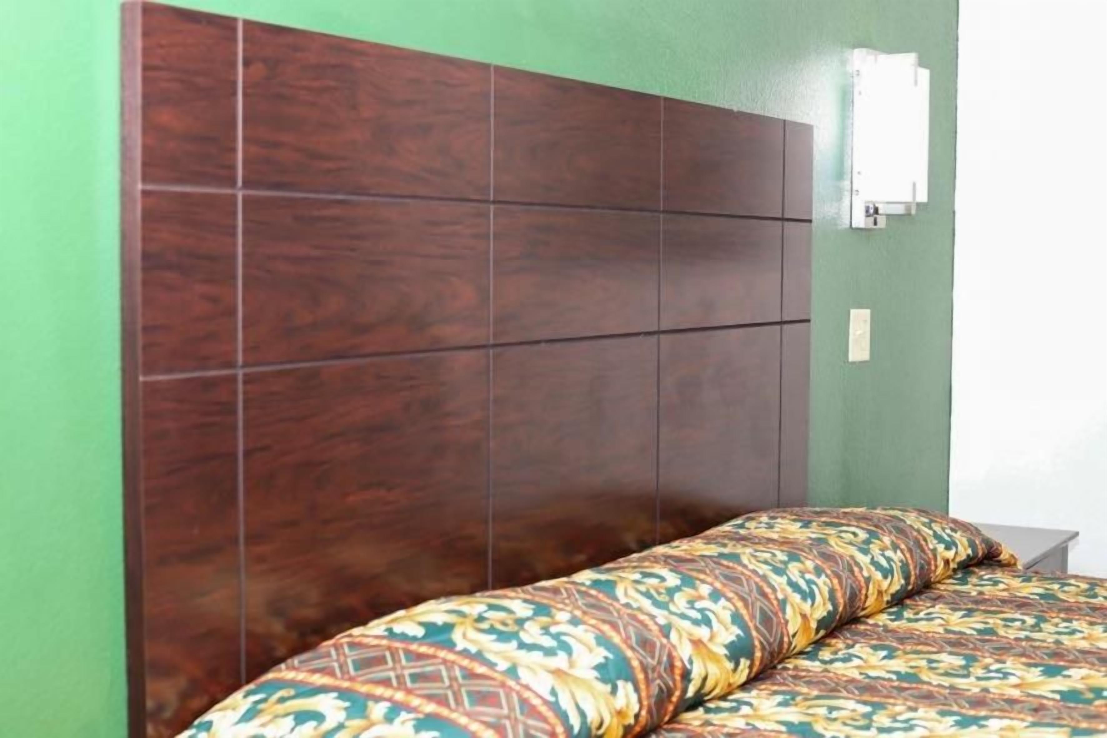 A bedroom with a wooden headboard, a patterned bedspread, and a wall-mounted electrical outlet.