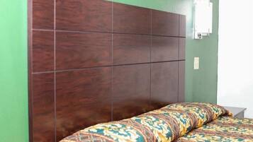 A bedroom with a wooden headboard, a patterned bedspread, and a wall-mounted electrical outlet.