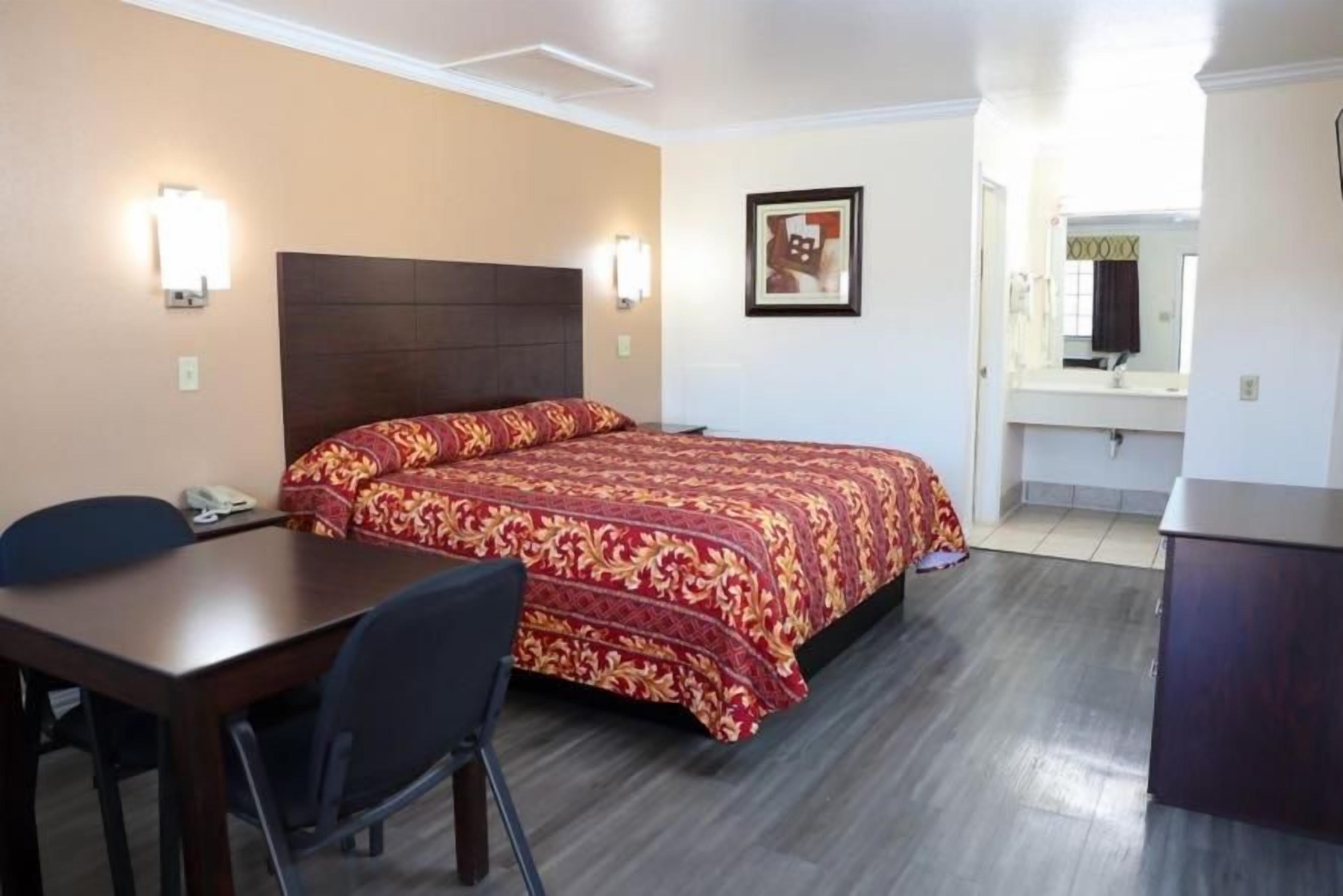 A hotel room with a bed, a desk, a chair, a phone, and a bathroom with a mirror and sink.