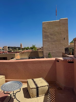 Una terraza en la azotea con una mesa y un reposapiés, una bandera y vistas a una mezquita con un minarete.