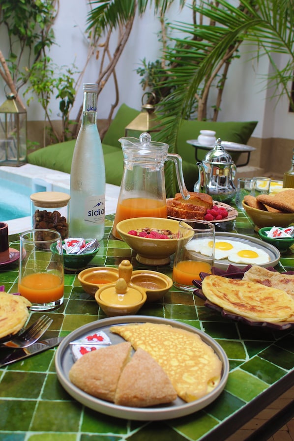 Un bufé de desayuno con diversos platos, incluyendo huevos, bollería y una botella de agua Sidral.