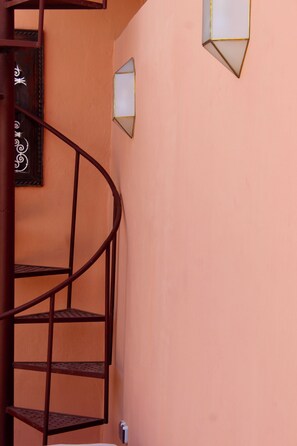 A spiral staircase with metal railings against a peach-colored wall, a decorative mirror, and two wall-mounted light fixtures. - Exceptional private riad with a pool in Mouassine, in the heart of the Medina (Marrakech)