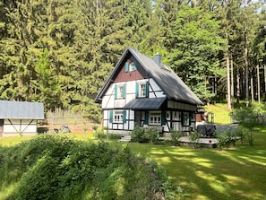 Una casa tradicional amb estructura de fusta i rajola, envoltada d'un jardí ben cuidat i un bosc dens.