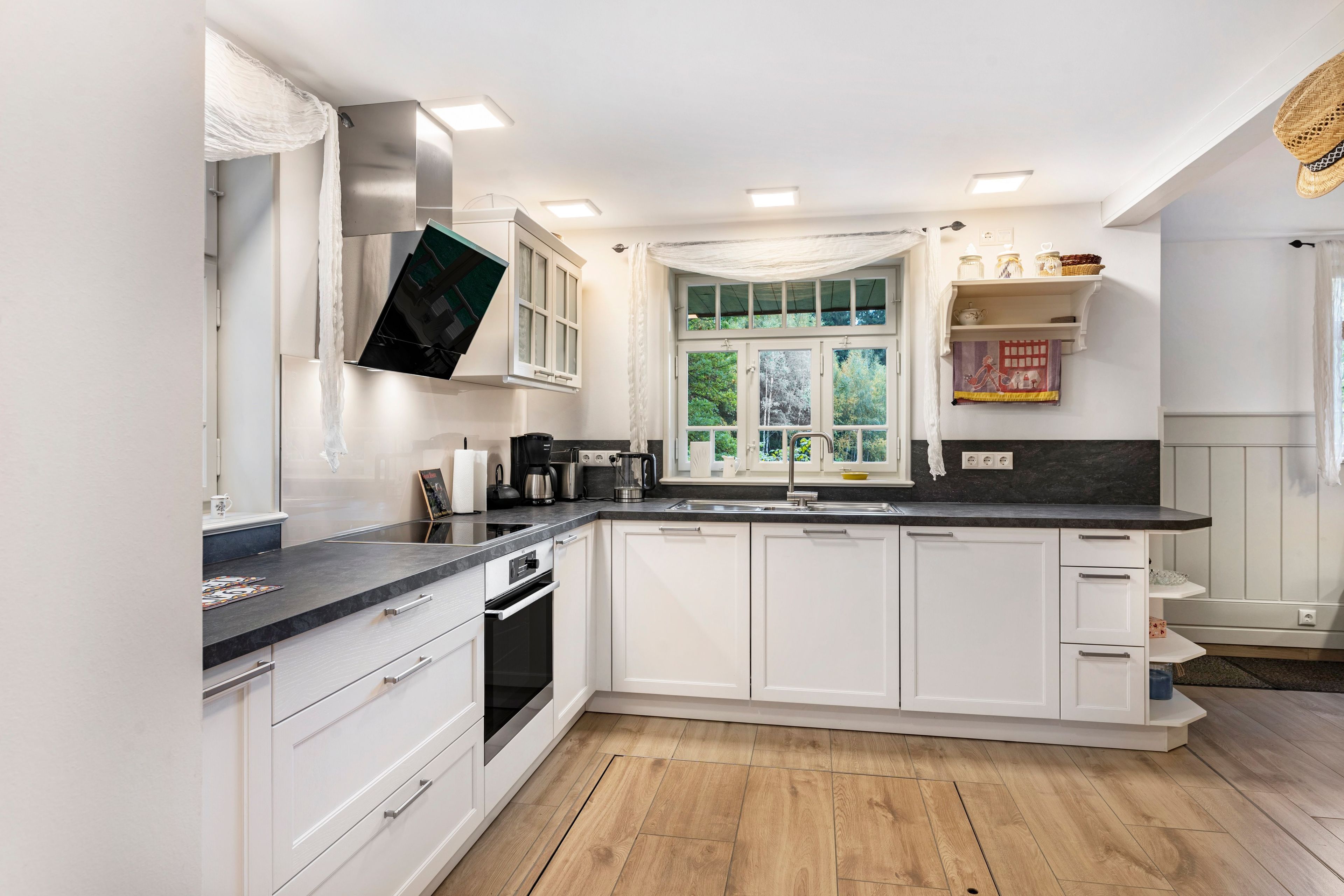 A modern kitchen with white cabinets, a black countertop, and a window with a view of greenery.