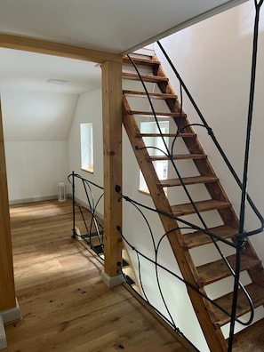 A wooden staircase with metal railings in a room with wooden flooring and white walls.