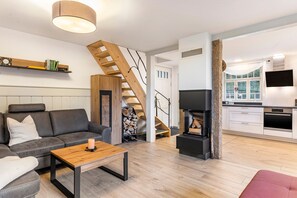 A modern living room with a sofa, coffee table, and fireplace. A staircase leads to a kitchen with a TV and oven.