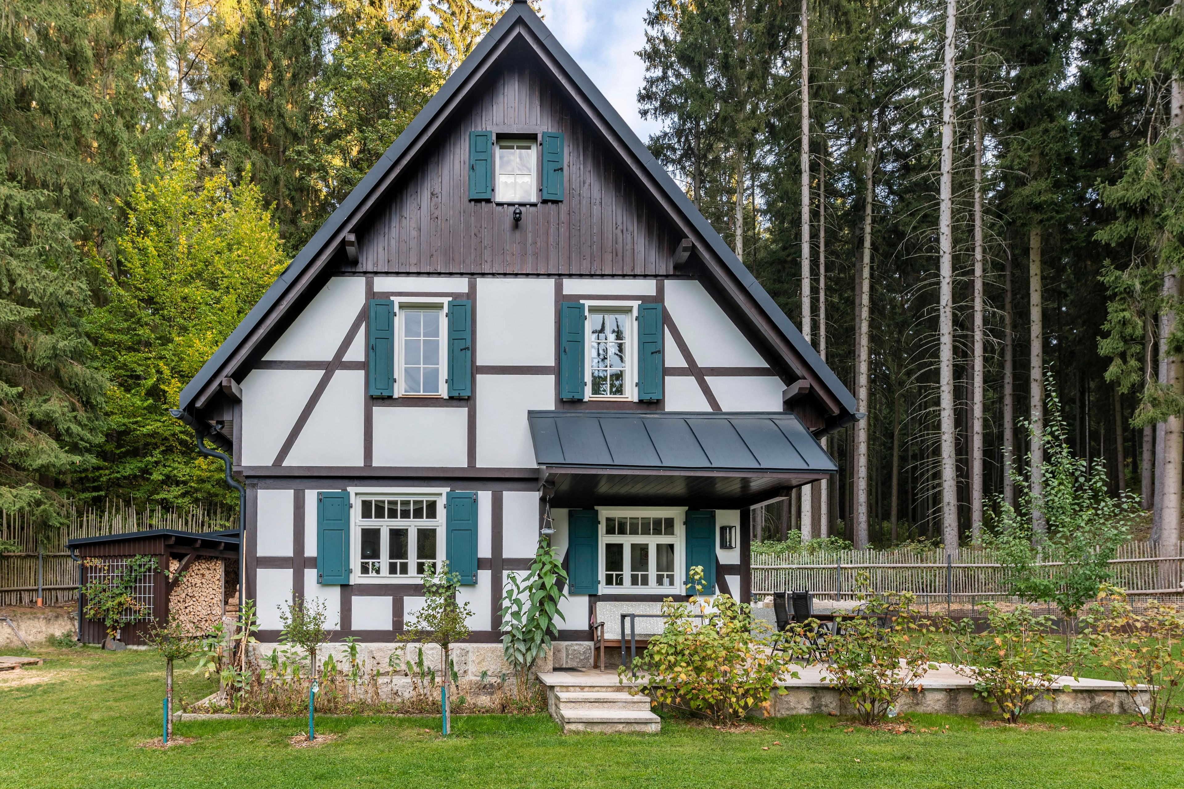 A traditional half-timbered house with a steep gable roof, surrounded by a forested area.