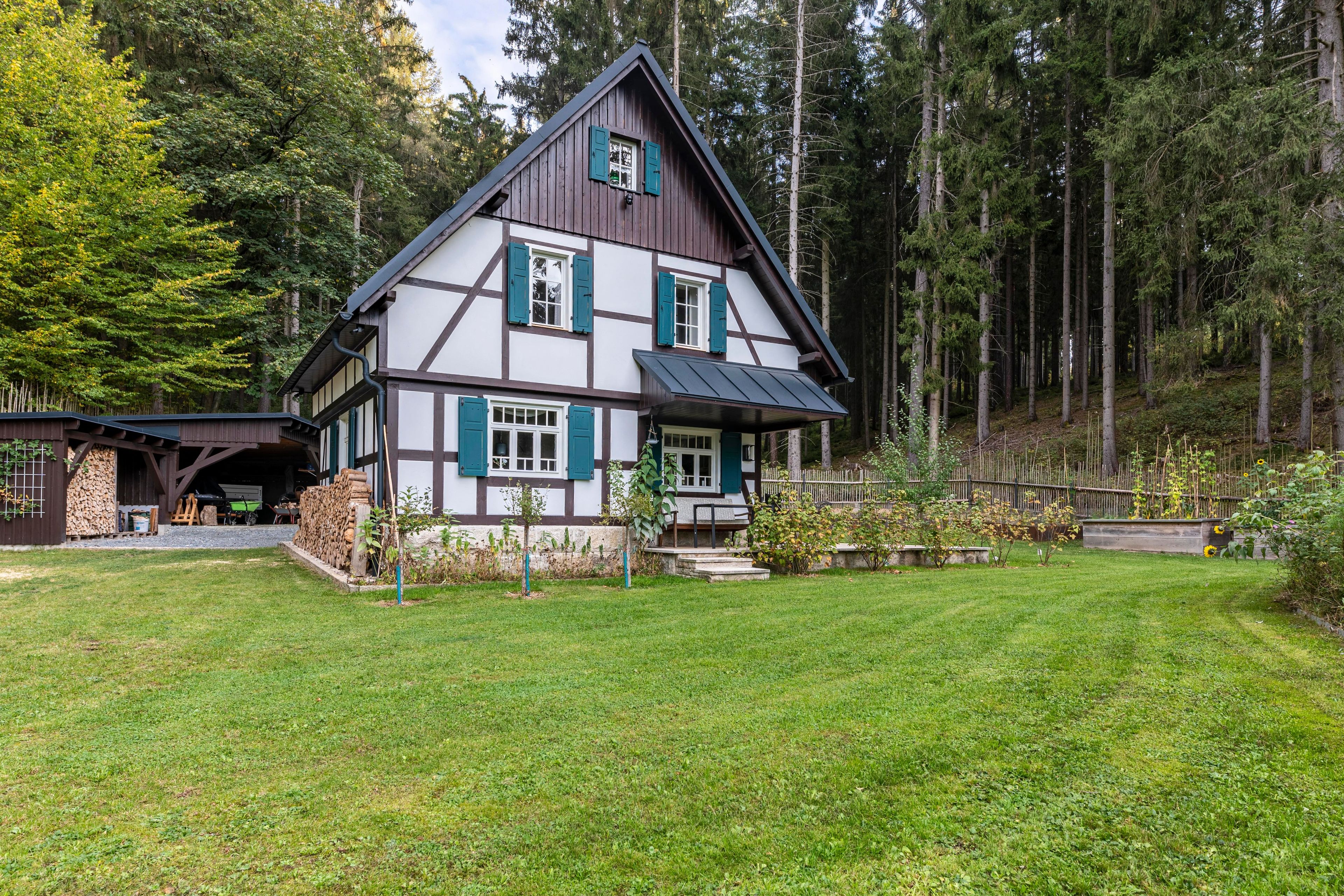 A two-story house with a steep gable roof, surrounded by a forest.