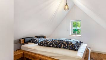 Un dormitorio con techo inclinado, cama con cabecera de madera, mesita de noche y ventana con vista a la vegetación.