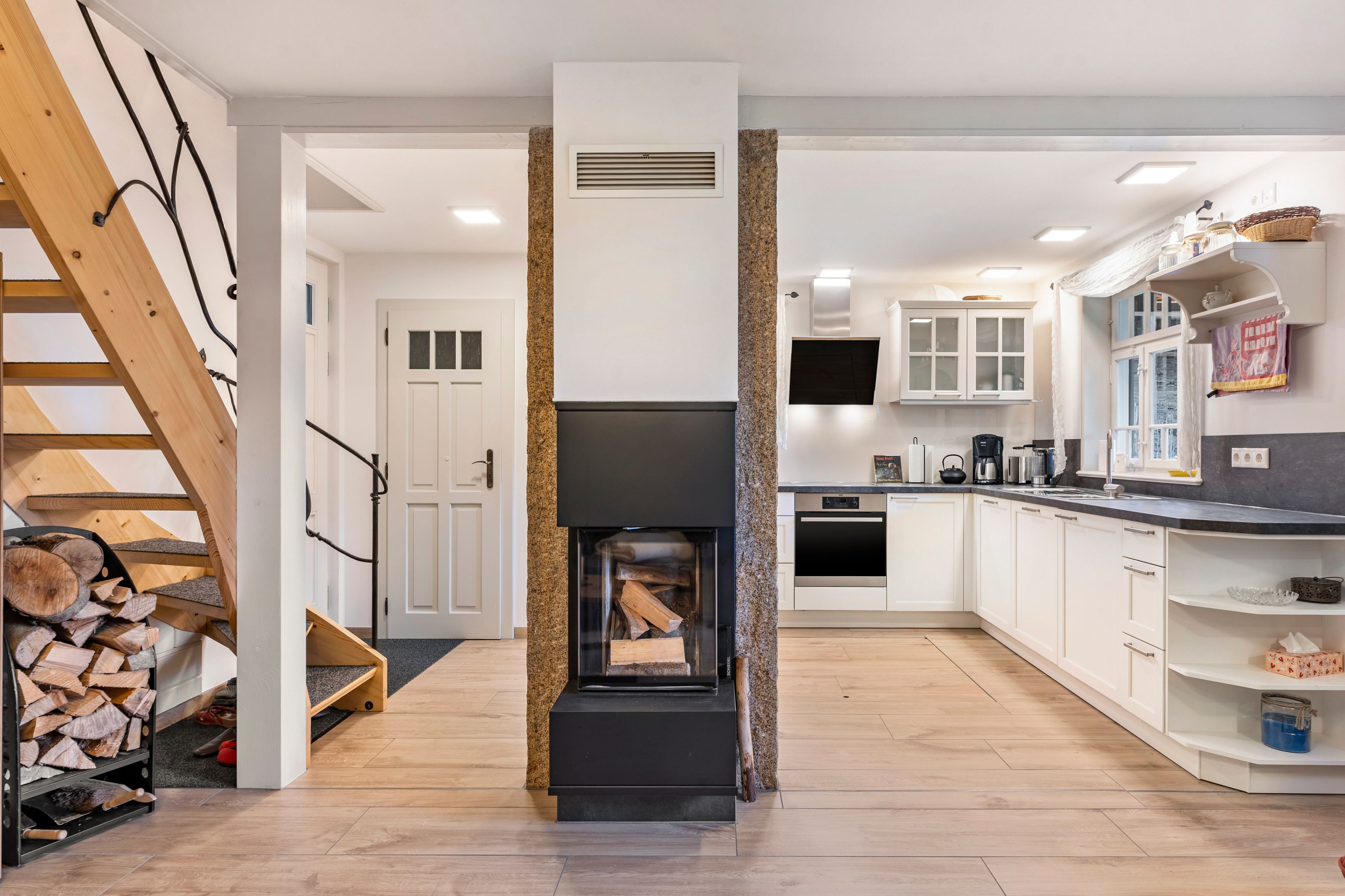 A modern kitchen with a built-in fireplace, wooden staircase, and white cabinetry.