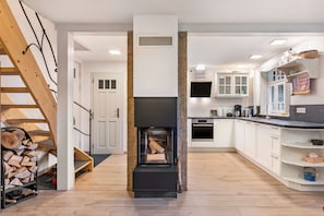 A modern kitchen with a built-in fireplace, wooden staircase, and white cabinetry.
