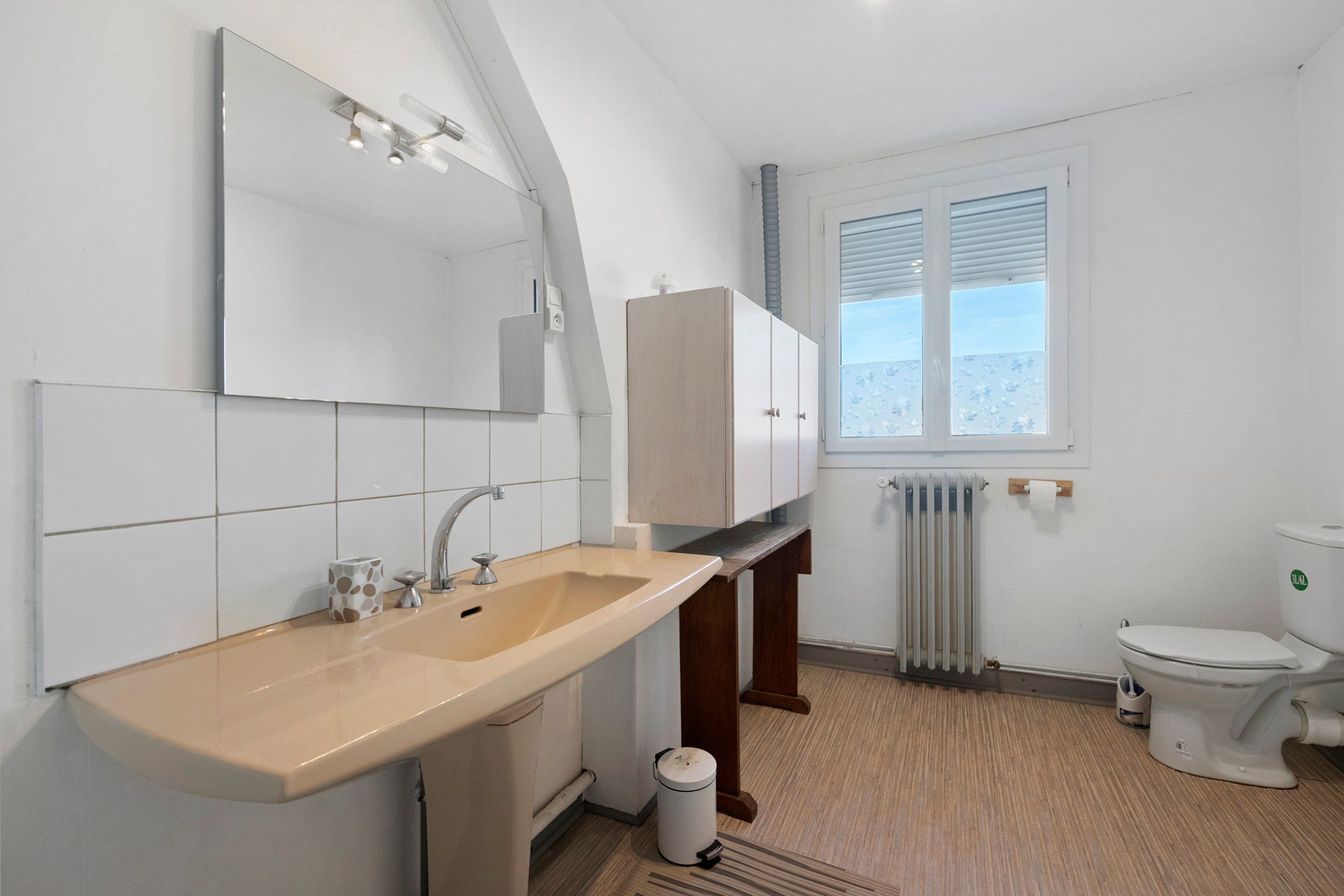 Ein modernes Badezimmer mit Waschbecken, Spiegel, Schränken, Toilette und einem Fenster.