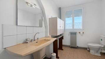 Ein modernes Badezimmer mit Waschbecken, Spiegel, Schränken, Toilette und einem Fenster.