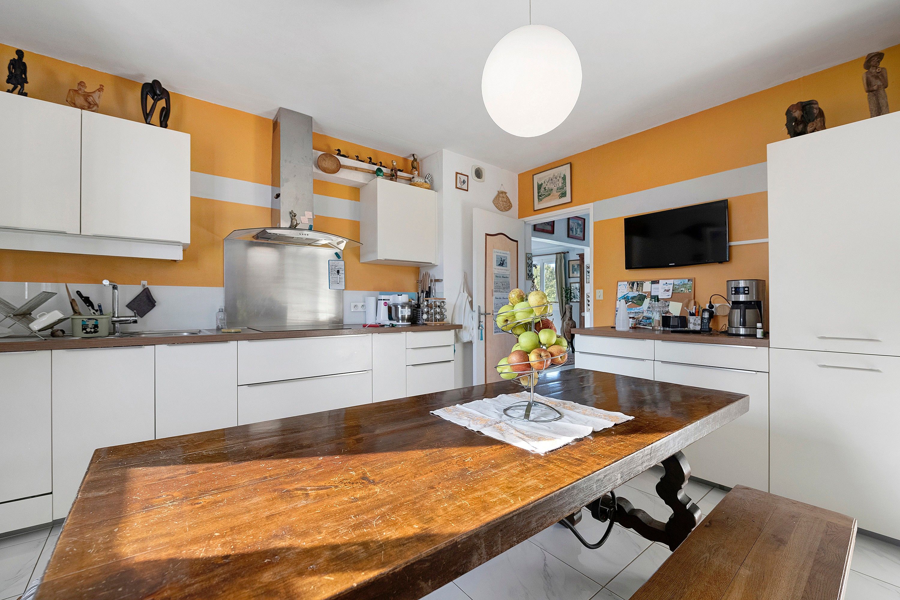 Een moderne keuken met witte kasten, een houten eiland en een flatscreen televisie boven de aanrecht.