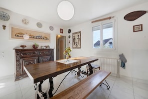 Een eethoek met een houten tafel en bank, een raam met uitzicht en diverse wanddecoraties.