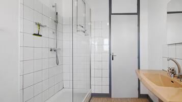 Ein Badezimmer mit weiß gefliesten Wänden, einer Dusche, einem Waschbecken und einer Tür.