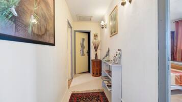 Un couloir avec un tapis à motifs, des œuvres d’art encadrées, une petite table en bois et une bibliothèque.