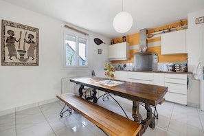 Una cocina con una mesa de madera, banco, armarios blancos y una lámpara colgante.