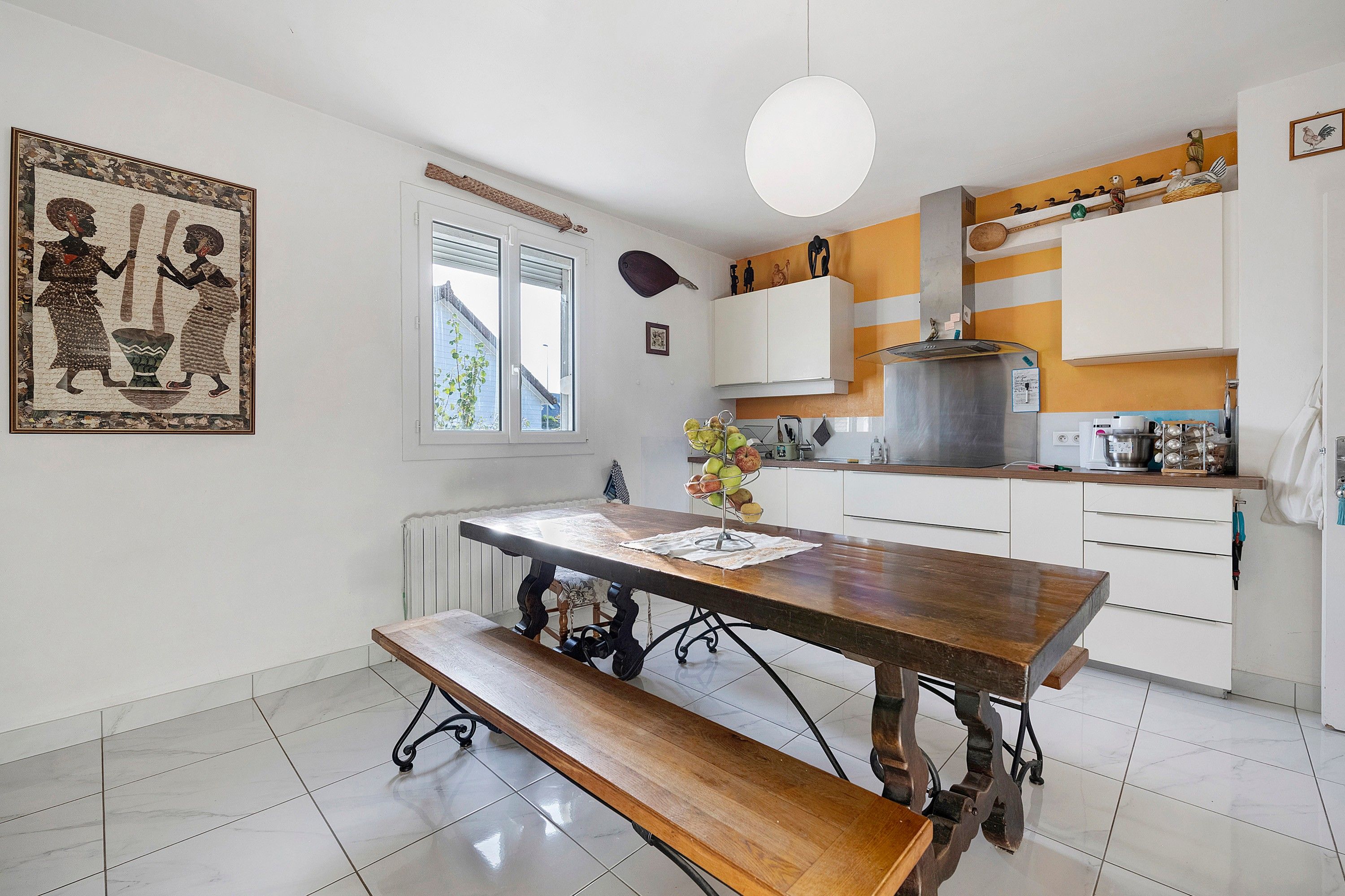 Une cuisine avec une table en bois, un banc, des armoires blanches et un luminaire suspendu.