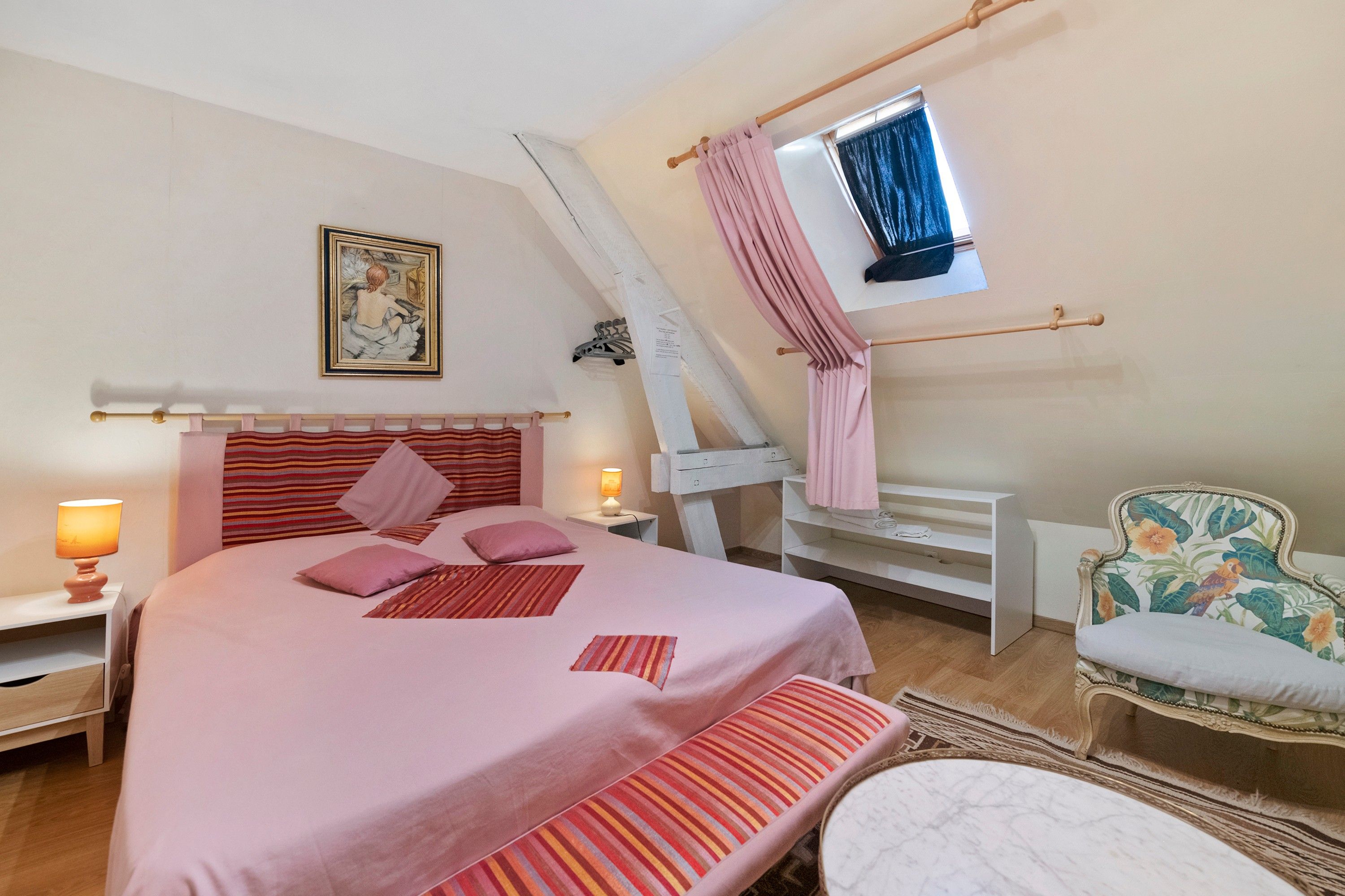 Ein Schlafzimmer mit einem Bett, Nachttischlampen, einem Sessel, einem Fenster mit Vorhängen und einem Bild an der Wand.