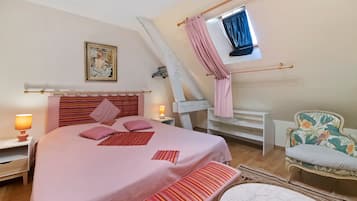 Ein Schlafzimmer mit einem Bett, Nachttischlampen, einem Sessel, einem Fenster mit Vorhängen und einem Bild an der Wand.