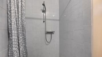 Eine Dusche mit Handbrause und Wandarmatur, ein Duschvorhang mit geometrischem Muster sowie ein gefliester Boden.