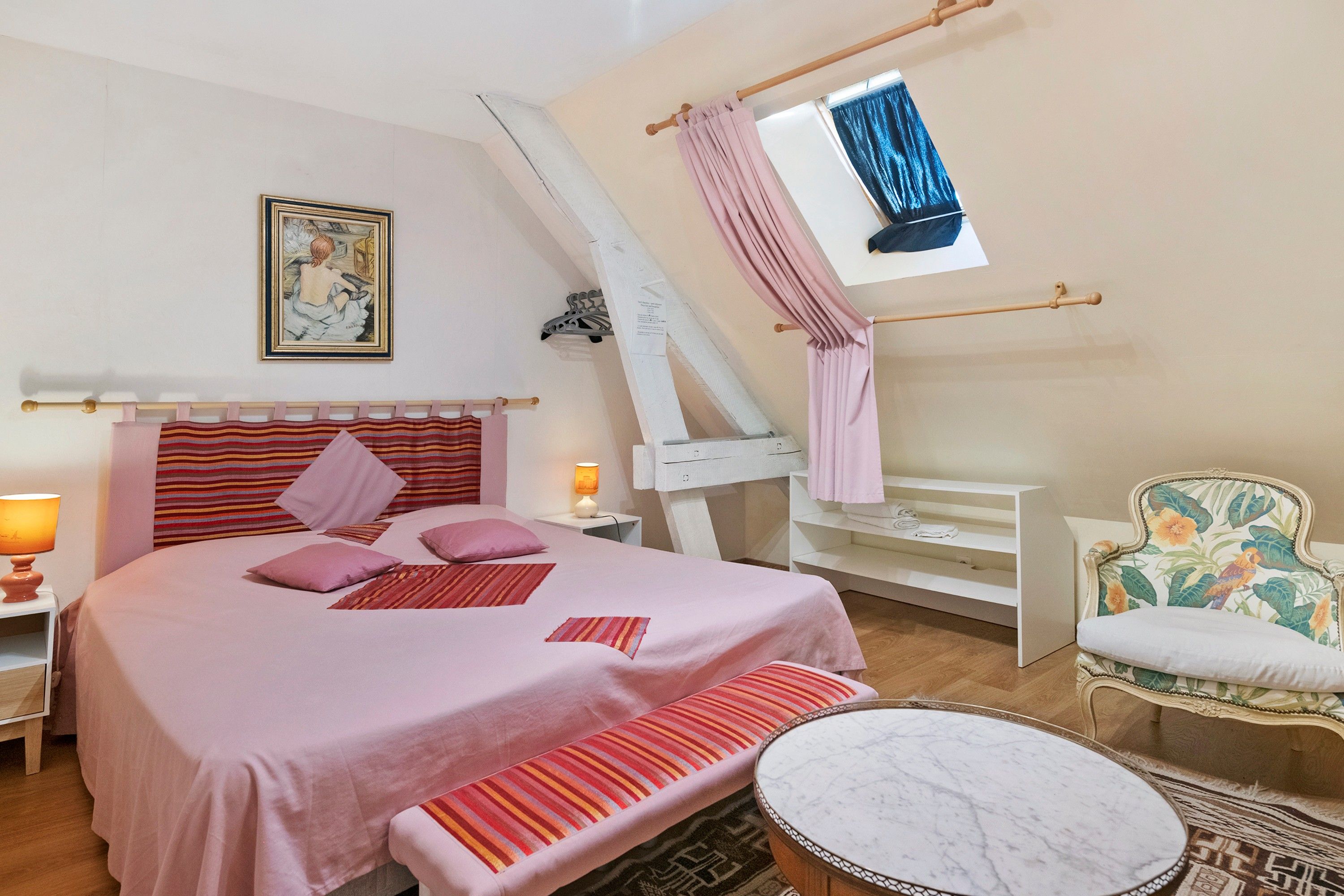 Ein Schlafzimmer mit einem Bett, Nachttischen, einer Bank, einem Sessel, einem Fenster mit Vorhängen und einem Bild an der Wand.