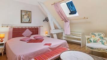 Ein Schlafzimmer mit einem Bett, Nachttischen, einer Bank, einem Sessel, einem Fenster mit Vorhängen und einem Bild an der Wand.