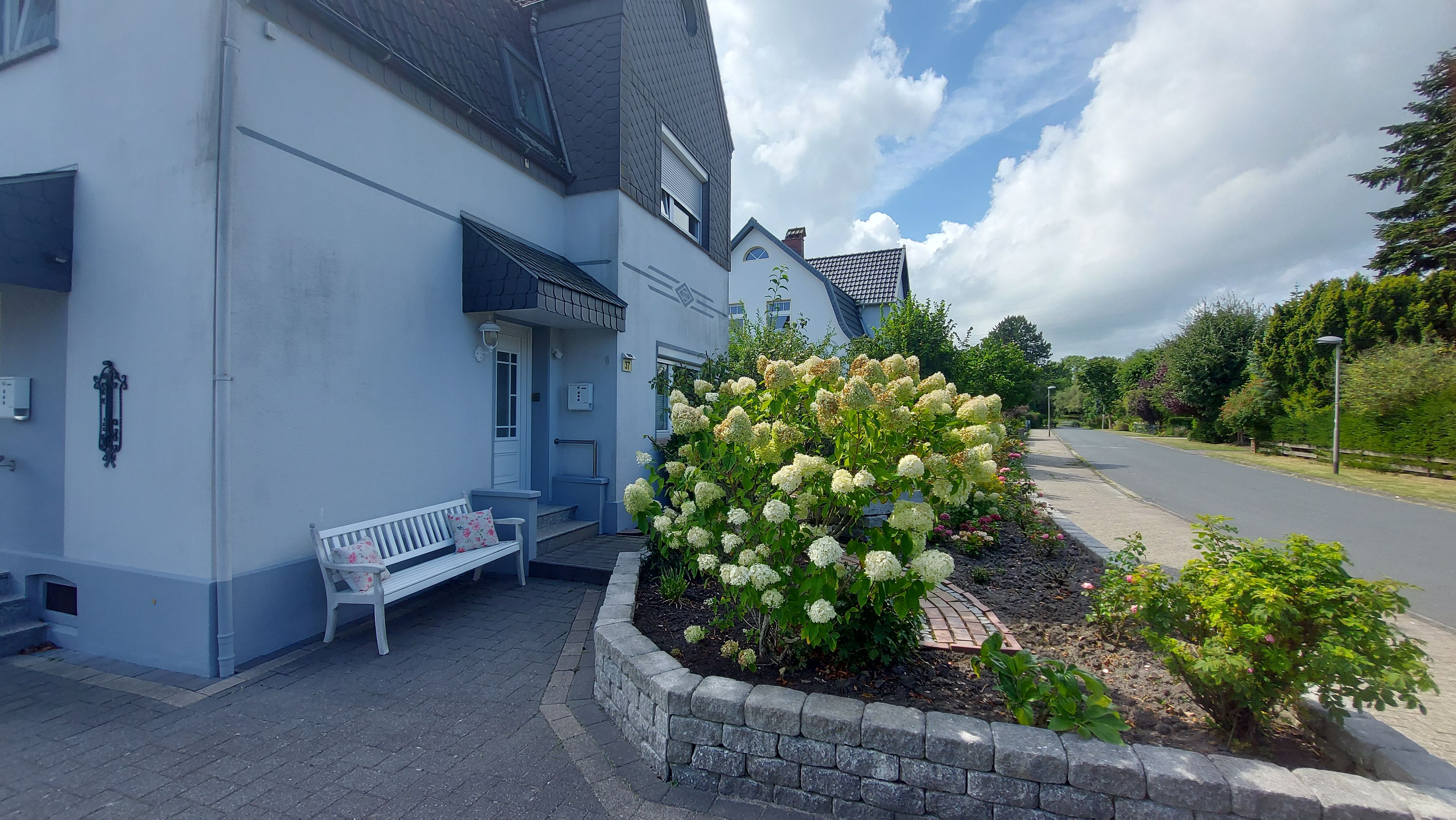 A building with a blue exterior, a bench outside, and a garden with white flowers.