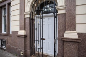 A building entrance with a white door, a black metal gate, and a sign above the door. - The Old Bank Vacant Nests Spacious 5BR (Newcastle)
