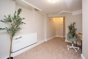 Une pièce avec un radiateur, un bureau avec une chaise et deux plantes en pot.