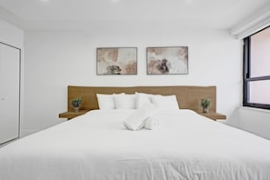 A modern bedroom with a large bed, two bedside tables with potted plants, and two abstract paintings on the wall. - Spacious 3BR Retreat Steps from the Beach with Resort Amenities 1508 (Miami Beach)