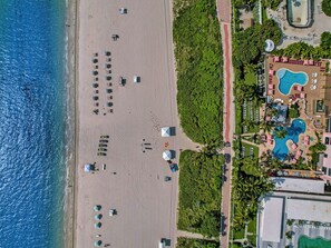 An aerial view of a beach resort with a swimming pool, sun loungers, and a beach area with umbrellas. - Spacious 3BR Retreat Steps from the Beach with Resort Amenities 1508 (Miami Beach)