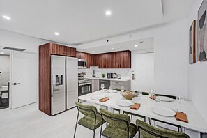 A modern kitchen with a dining area, featuring a stainless steel refrigerator, microwave, oven, and a white countertop. - Spacious 3BR Retreat Steps from the Beach with Resort Amenities 1508 (Miami Beach)