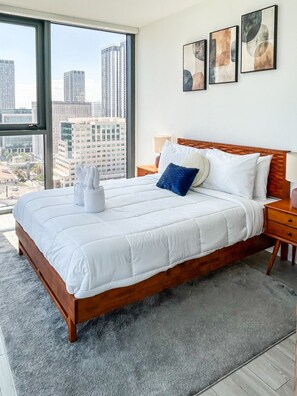 Ein Hotelzimmer mit einem großen Bett, Blick auf die Stadt und drei gerahmten Kunstwerken an der Wand.