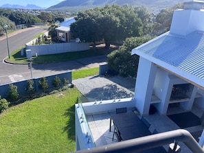 A residential building with a flat roof, a covered patio area, and a view of a road and greenery. - Gorgeous 4-bedroom house in charming Onrusrivier perfect for families. (Onrusrivier)