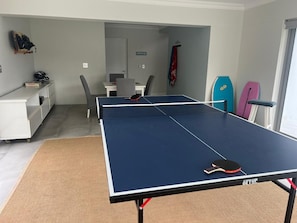 A ping pong table in a room with a desk, chair, and surfboards against the wall. - Gorgeous 4-bedroom house in charming Onrusrivier perfect for families. (Onrusrivier)