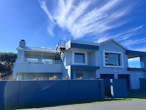 Ein modernes, zweistöckiges Haus mit blauer Fassade und einer sichtbaren Treppe, bewölkter Himmel.