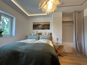 Ein Schlafzimmer mit einem Bett, einem Gemälde, einem Fenster und einer Deckenleuchte.
