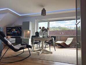 Ein modernes Wohnzimmer mit Fernseher, Sitzgelegenheiten, einem Essbereich und Blick ins Freie.