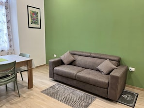 Ein Wohnzimmer mit einem braunen Sofa, einem Esstisch mit Stühlen, einer grünen Wand und einem gerahmten Bild.
