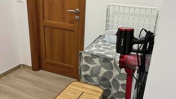 A room with a wooden door, a patterned bed, a red hairdryer, and a wicker basket on the floor.