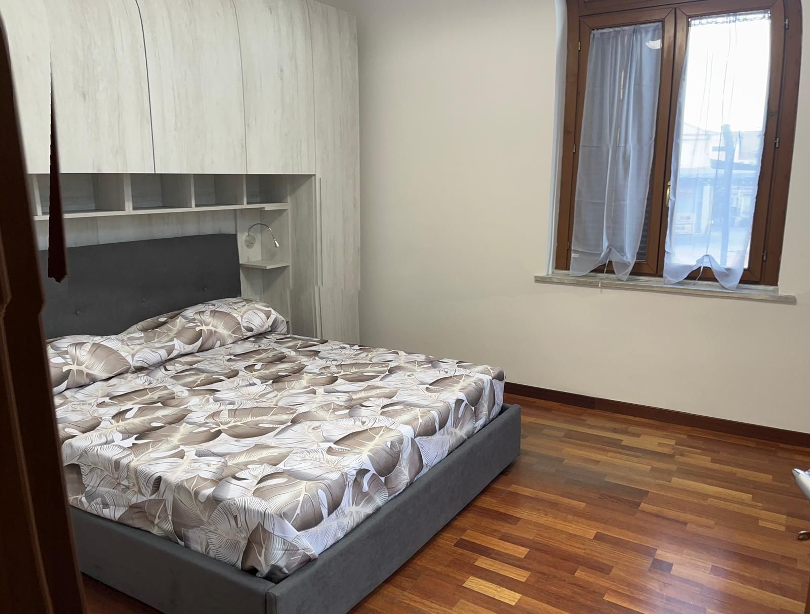 A bedroom with a bed, a window with curtains, and a wooden floor.