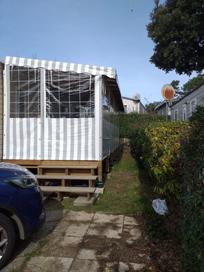 Una casa móvil con un toldo a rayas, una terraza de madera y una antena parabólica.
